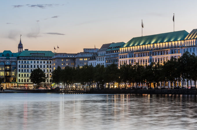 Evening view of the exterior of the Fairmont Hotel Vier Jahreszeiten along the waterfront promenade.