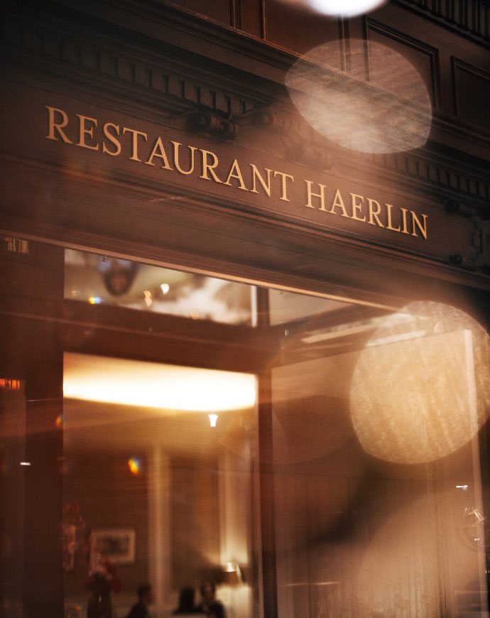 The warmly lit entrance to Restaurant Haerli*** with elegant golden lettering.